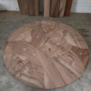 Round tabletop of numbered eucalyptus puzzle pieces laid out on the shop floor before the copper inlay